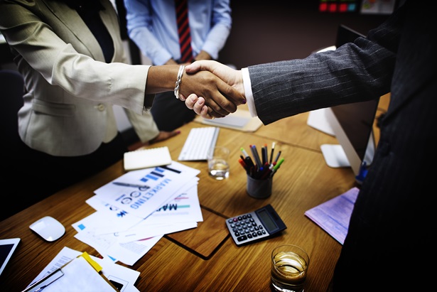 Diverse group of individuals gathered around a table shaking hands.