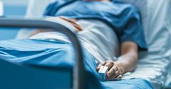 Patient in medical gown in their hospital bed with a Fingertip Pulse Oximeter attached to their finger