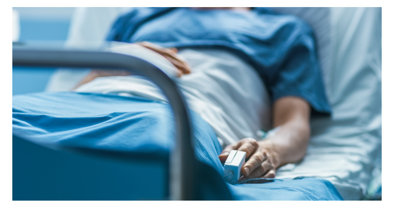 Patient in medical gown in their hospital bed with a Fingertip Pulse Oximeter attached to their finger