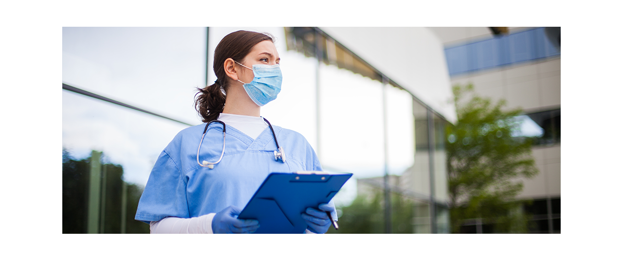 Clinician with surgical mask and clip board standing outside of health system