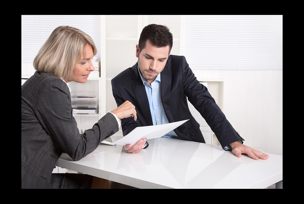 A man and woman in business suits sit at a table reviewing a document